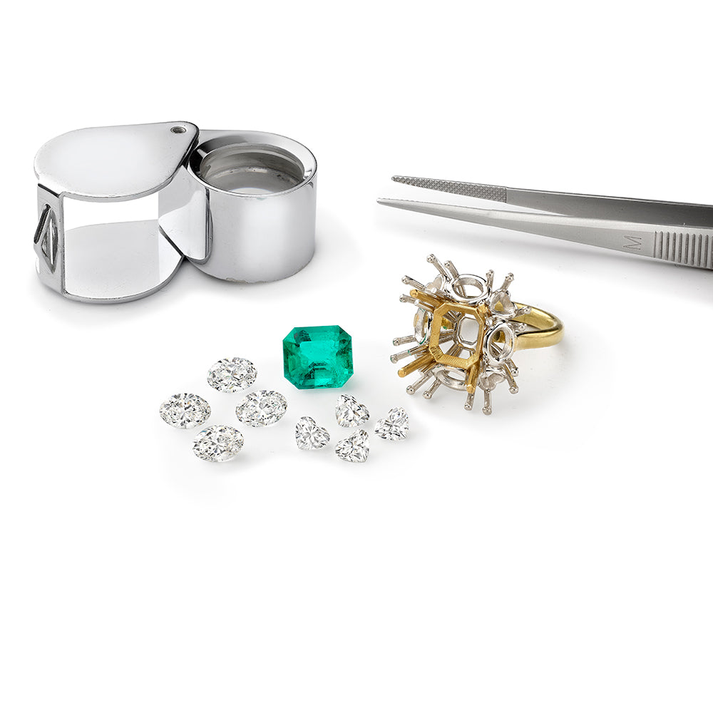 Emerald with diamonds and platinum and yellow gold ring shank in workshop with loupe and tweezers