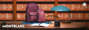 Burgundy leather backpack and crossbody bag on desk with a pen holder and 3 Montblanc pens.